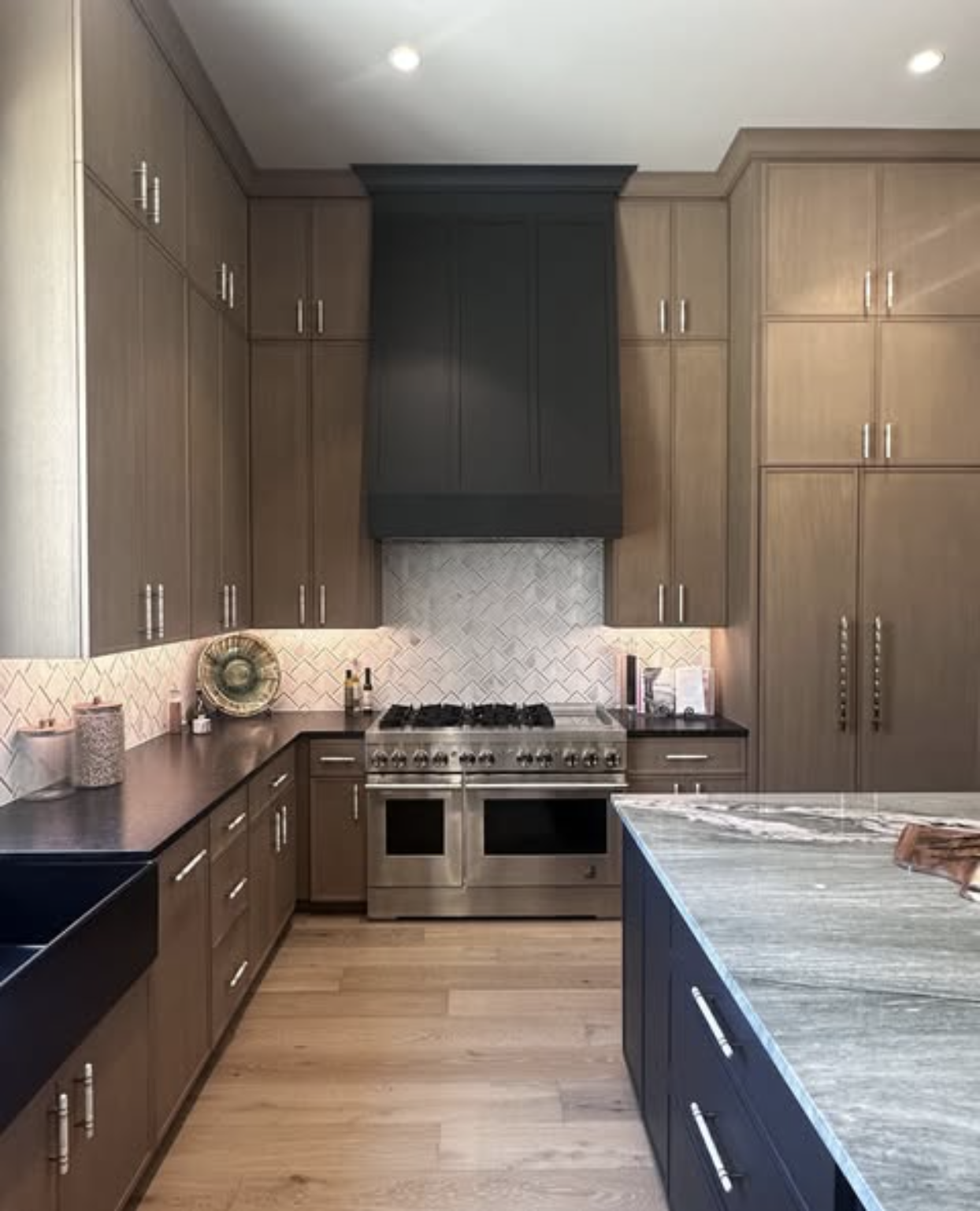 Two-tone rift-sawn oak kitchen with black shaker hood and navy quartzite island by Amaya