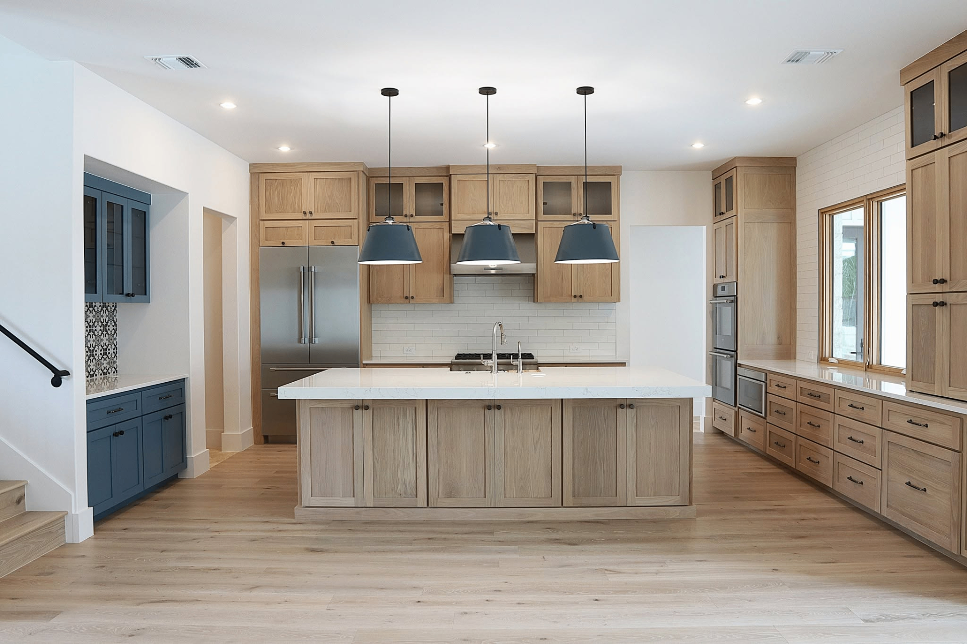 Open concept white oak kitchen with navy blue accents by Amaya