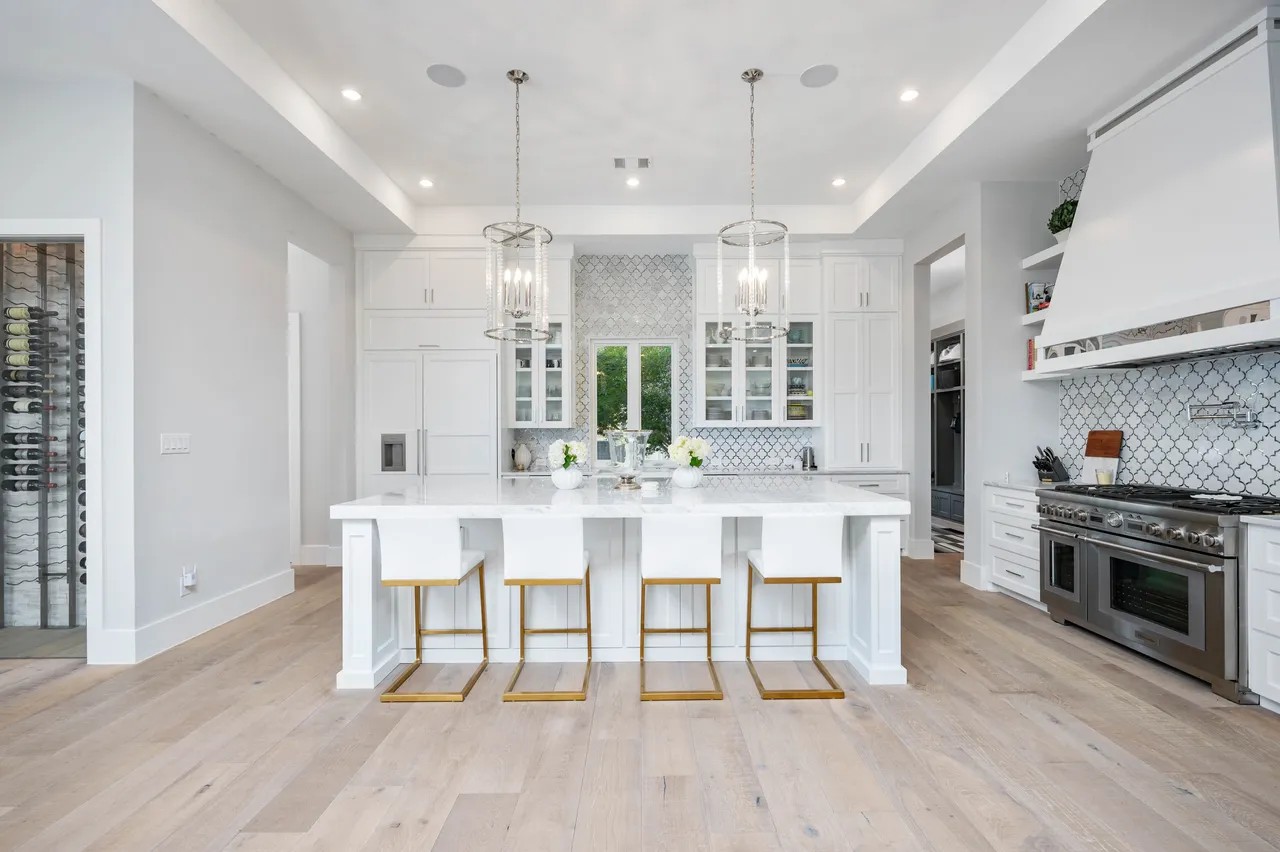 Bright white custom kitchen with arabesque tile backsplash, marble island, and integrated wine wall by Amaya