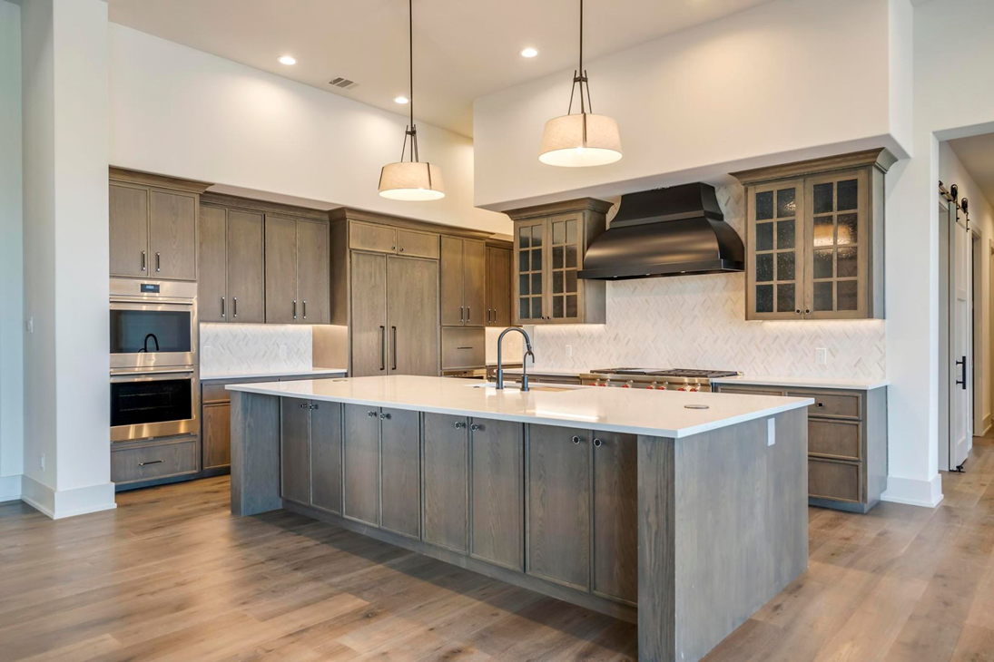 Rift-sawn white oak kitchen with a large stone-topped island, herringbone tile, and blackened steel range hood by Amaya