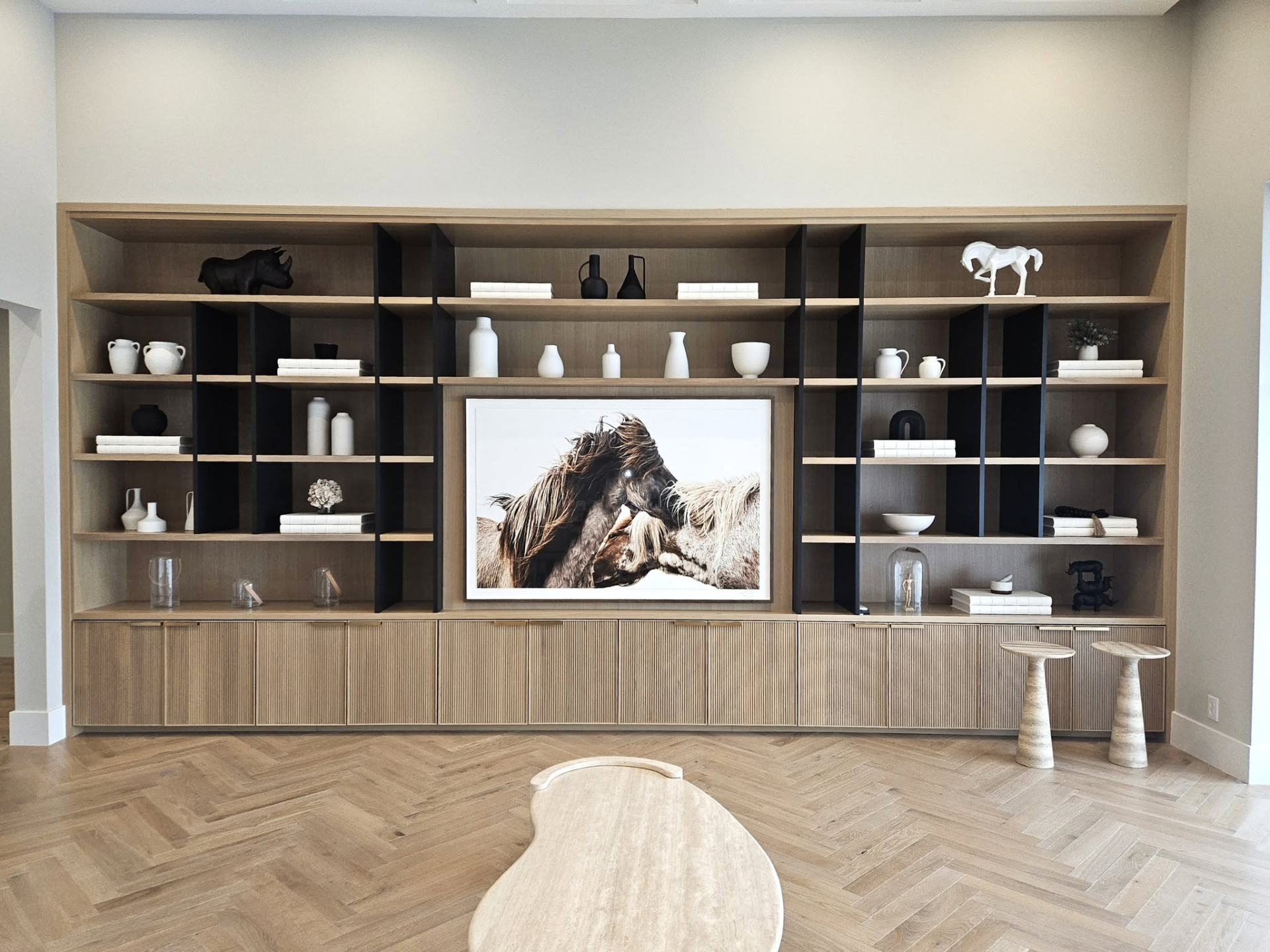 Floor-to-ceiling white oak and obsidian built-in shelving with frameless reeded doors by Amaya